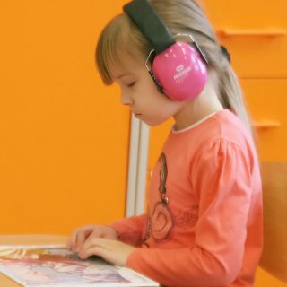 Zdjęcie dziecka w słuchawkach siedzącego przy stoliku.